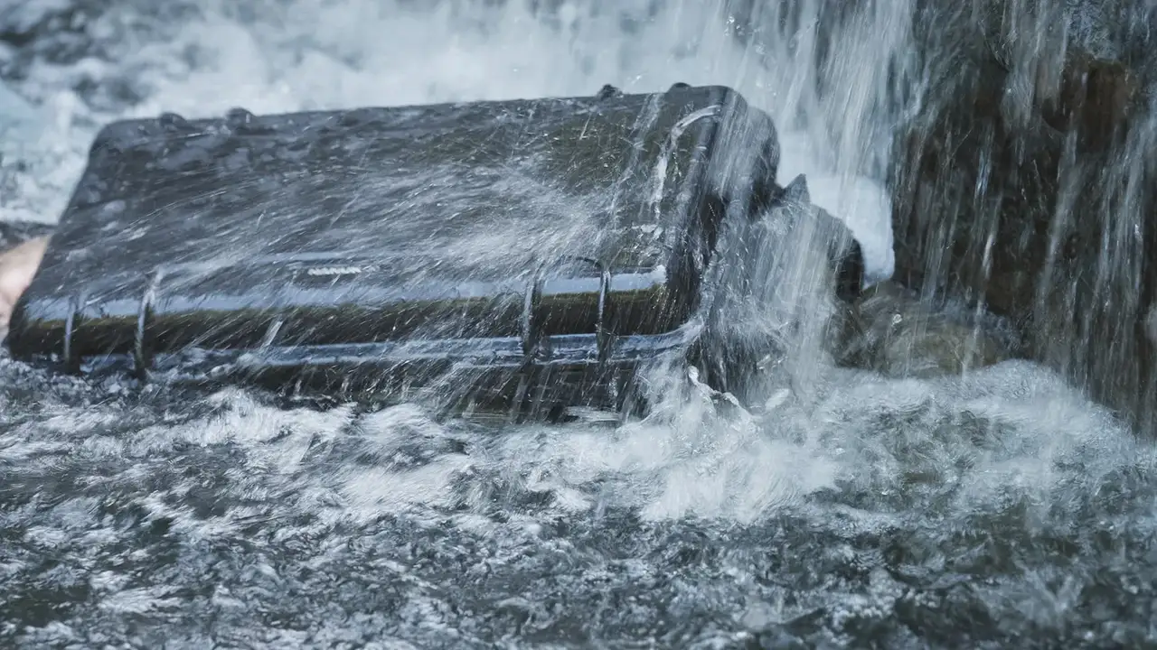 Black suitcase being submerged in water with a strong current