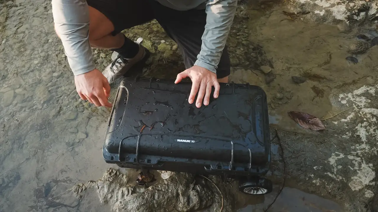 Person opening a black suitcase on a rocky surface