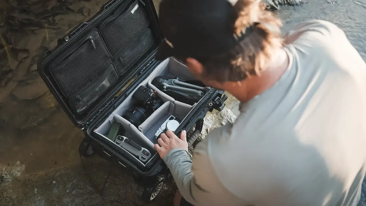 Person organizing items in a large black travel case outdoors.