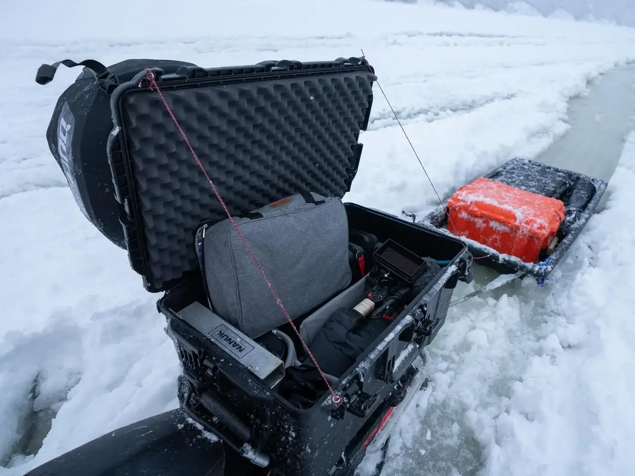 Ice fishing setup with a black fishing chair, rod, and red cooler on a frozen lake.
