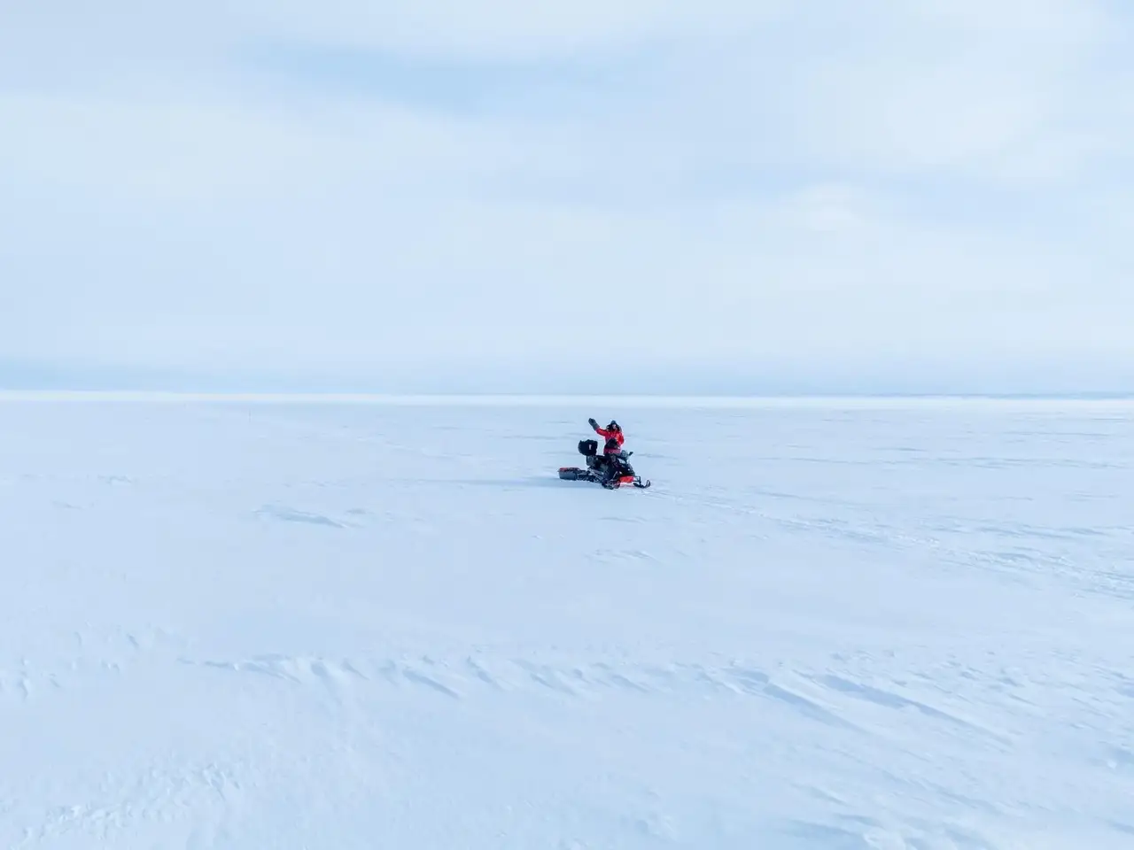 Person on a snowmobile in a vast snowy landscape with a clear blue sky.