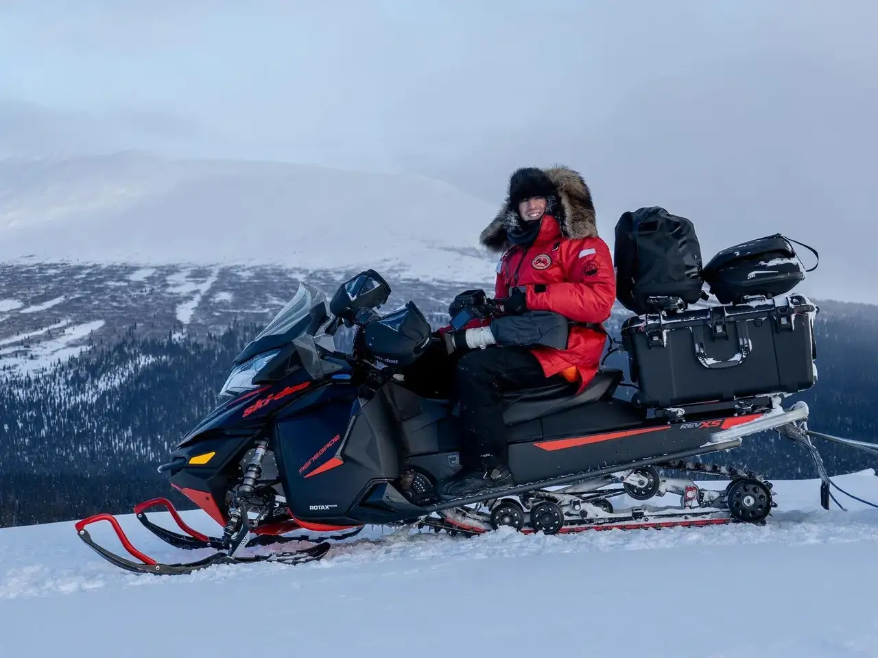 Person sitting on a snowmobile in a snowy landscape with mountains in the background