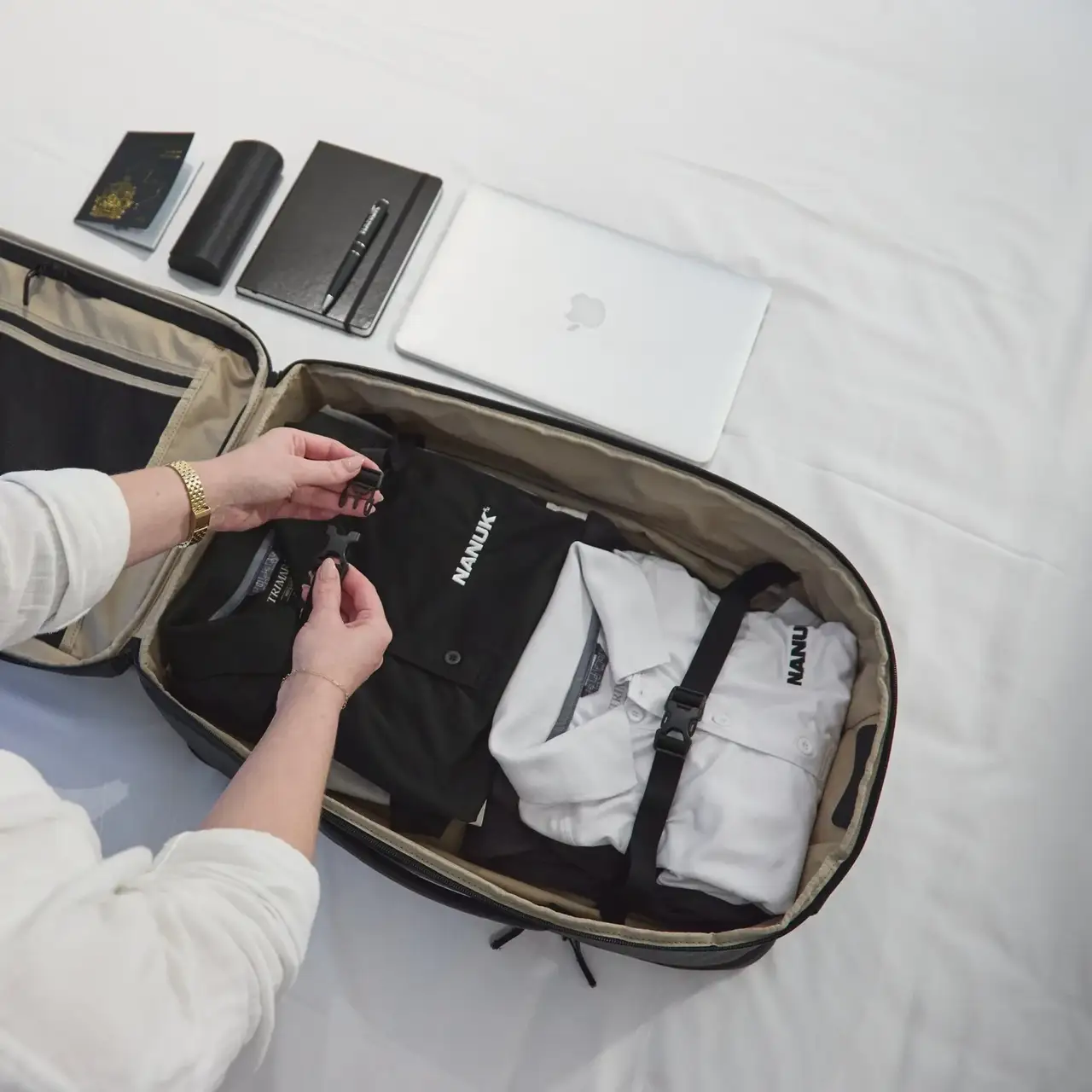 Person packing a suitcase with clothes and electronic devices on a bed