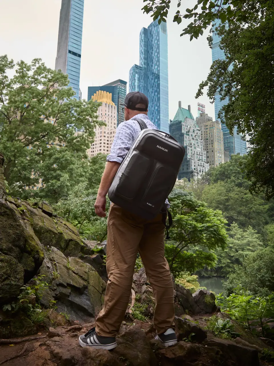 Person with a suitcase standing on a rocky outcrop with city skyline in the background