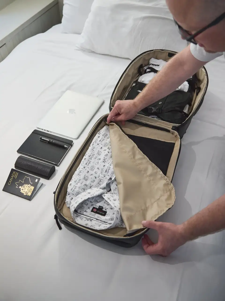 Person packing a suitcase on a bed with a smartphone and passport visible.