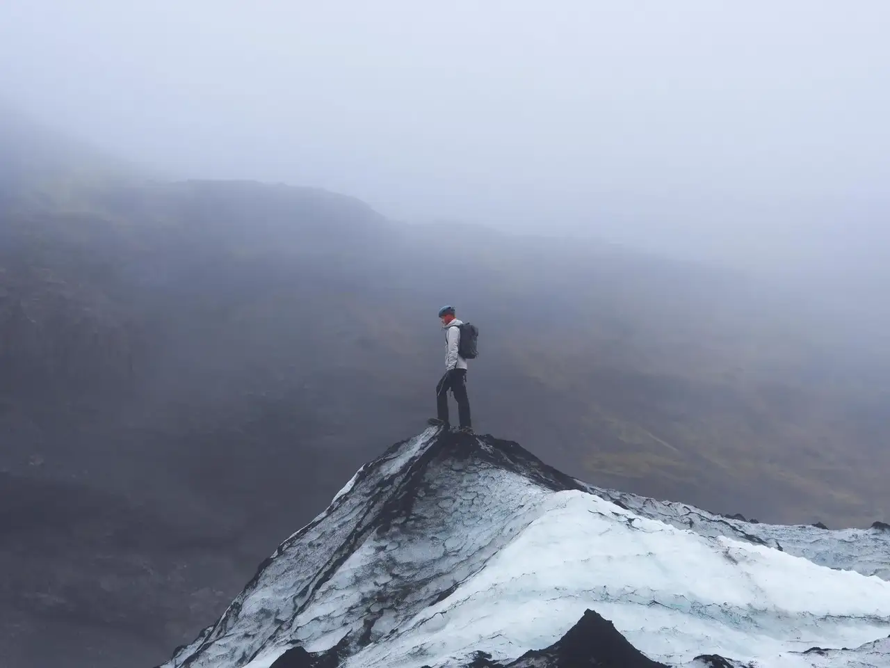 Person standing on a mountain peak with a backpack, surrounded by foggy landscape