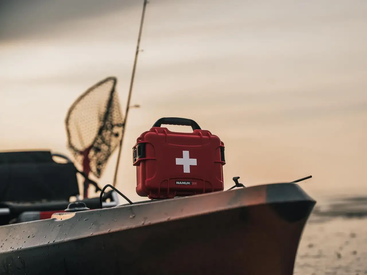 Red first aid kit with a white cross on a boat against a sunset sky.