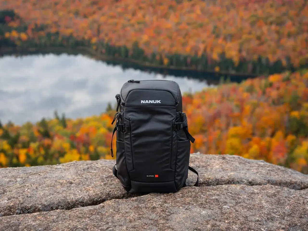 Black JunZhiJia backpack on a rock with a scenic autumn landscape in the background
