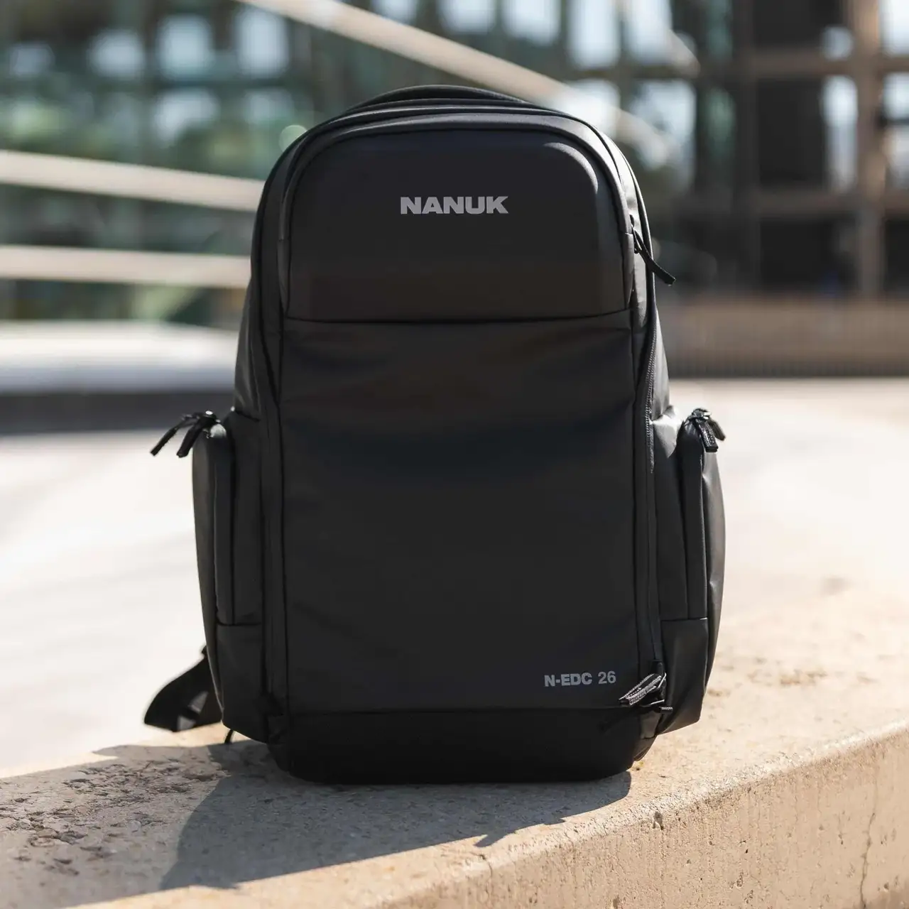 Black JunZhiJia backpack on a concrete ledge with a blurred background
