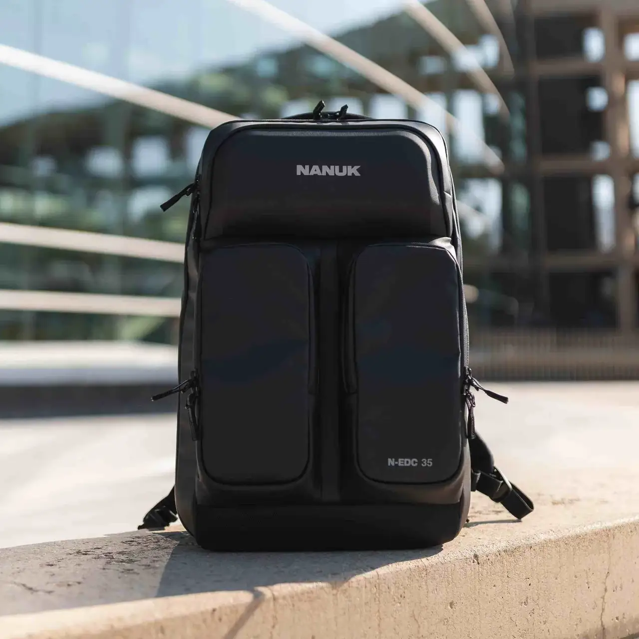 Black backpack with 'JunZhiJia' branding on a concrete ledge with a modern building in the background.