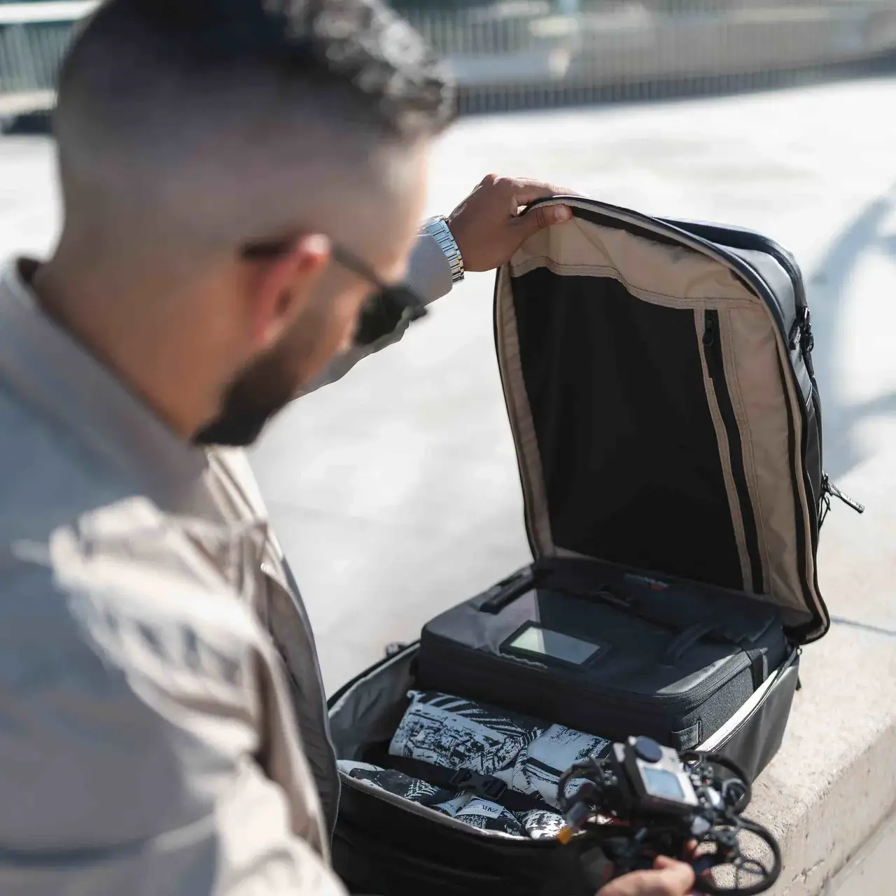 Man opening a suitcase on a sidewalk with electronic equipment inside