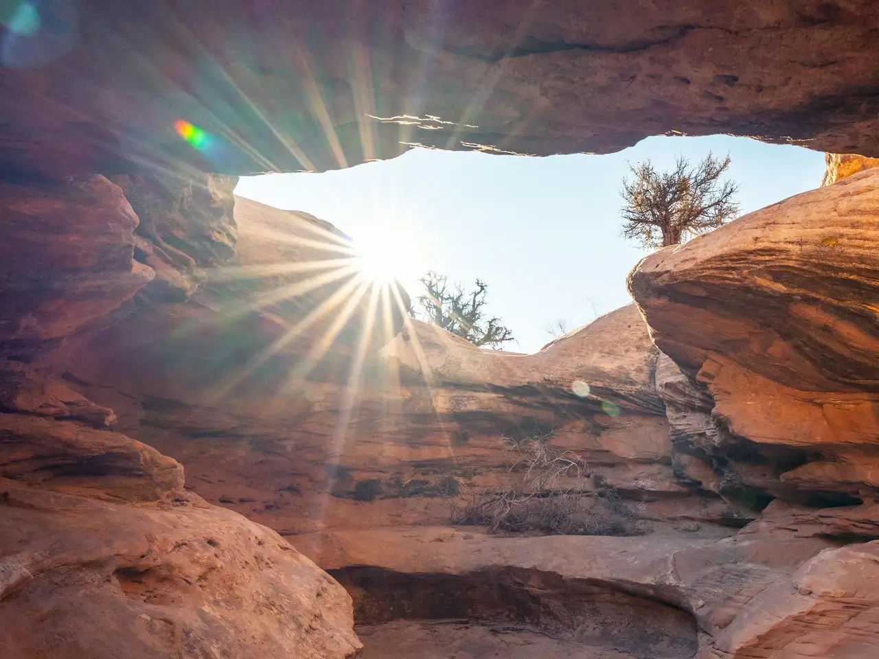 Sun shining through a natural rock arch in a desert landscape