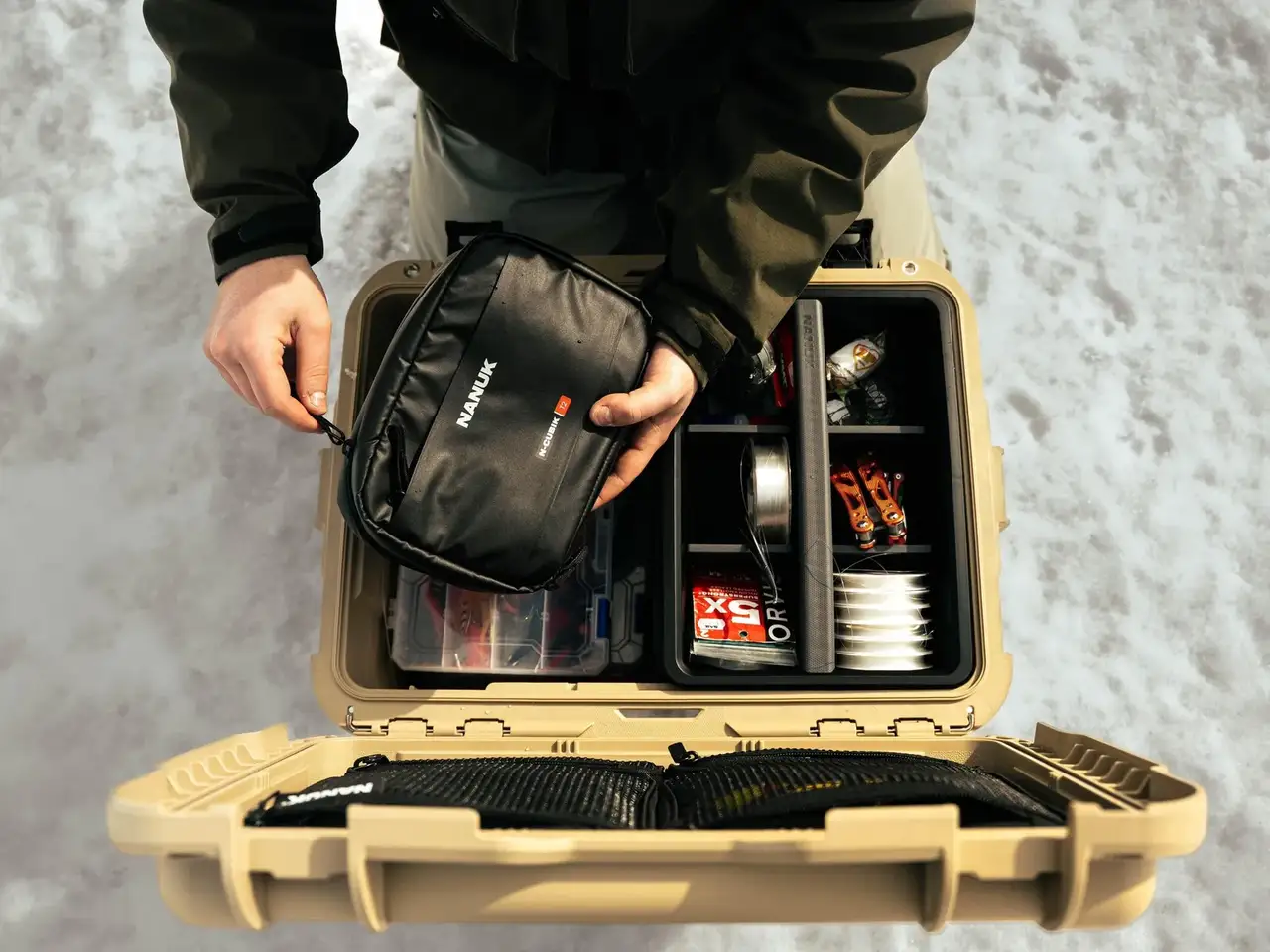 Person opening a beige tackle box filled with fishing gear against a snowy background