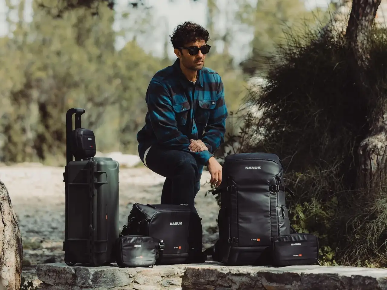 Man sitting outdoors with various camera bags and equipment