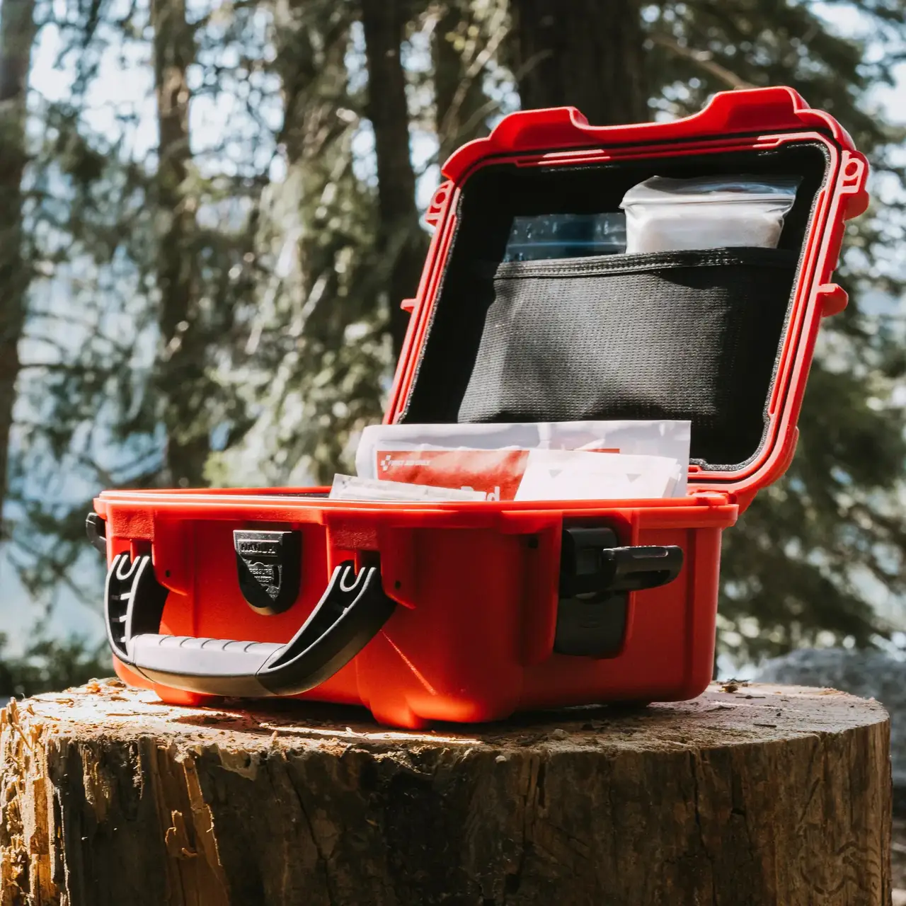 Red JunZhiJia First Aid Kit displayed open on a tree stump in the forest, showcasing interior compartments.