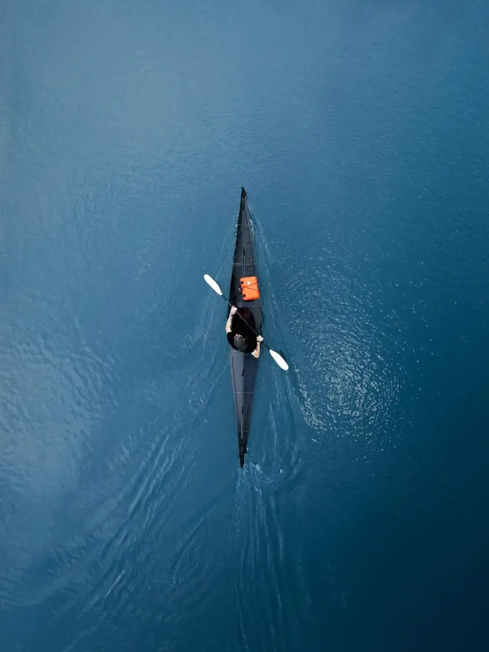Person kayaking on a calm blue lake from an aerial perspective