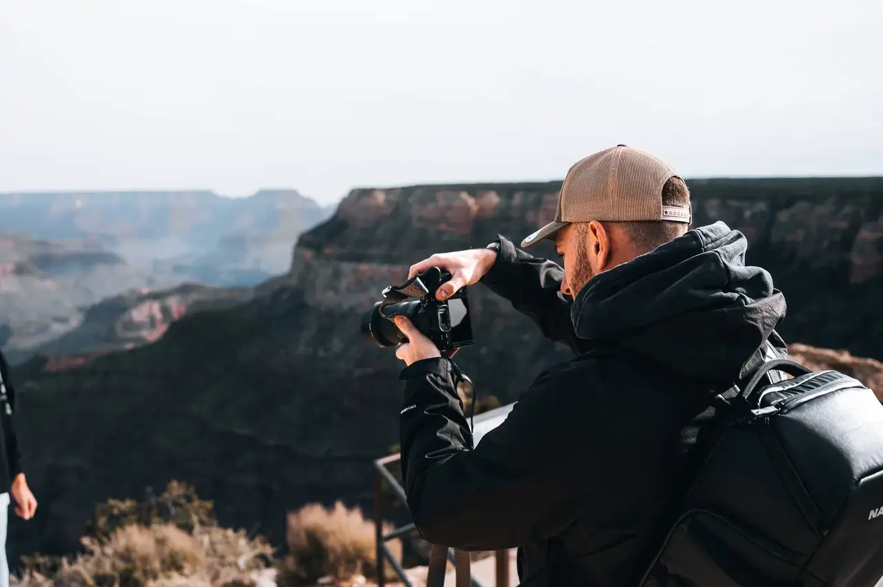Person taking a photograph of a scenic landscape with mountains in the background