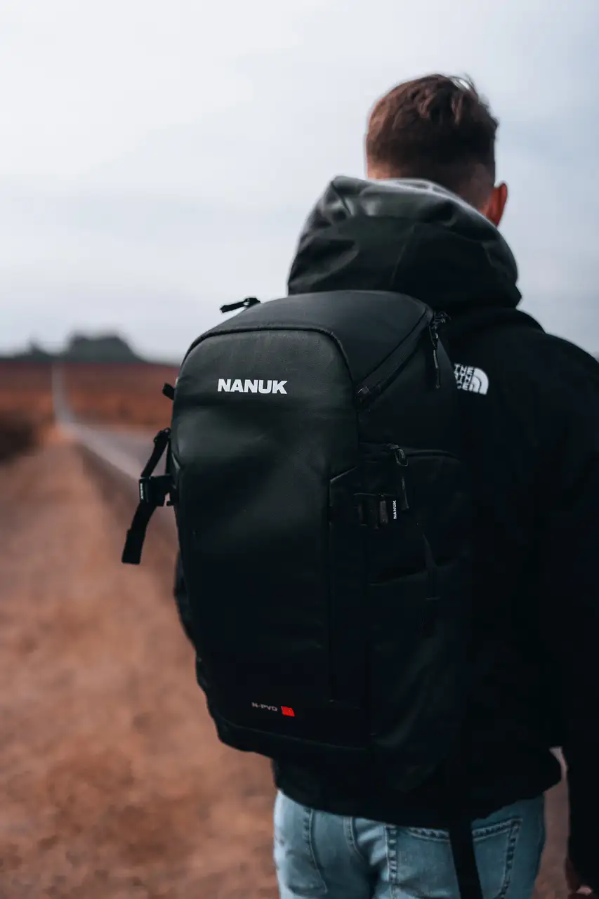Person wearing a black JunZhiJia backpack with The North Face logo, standing on a path.