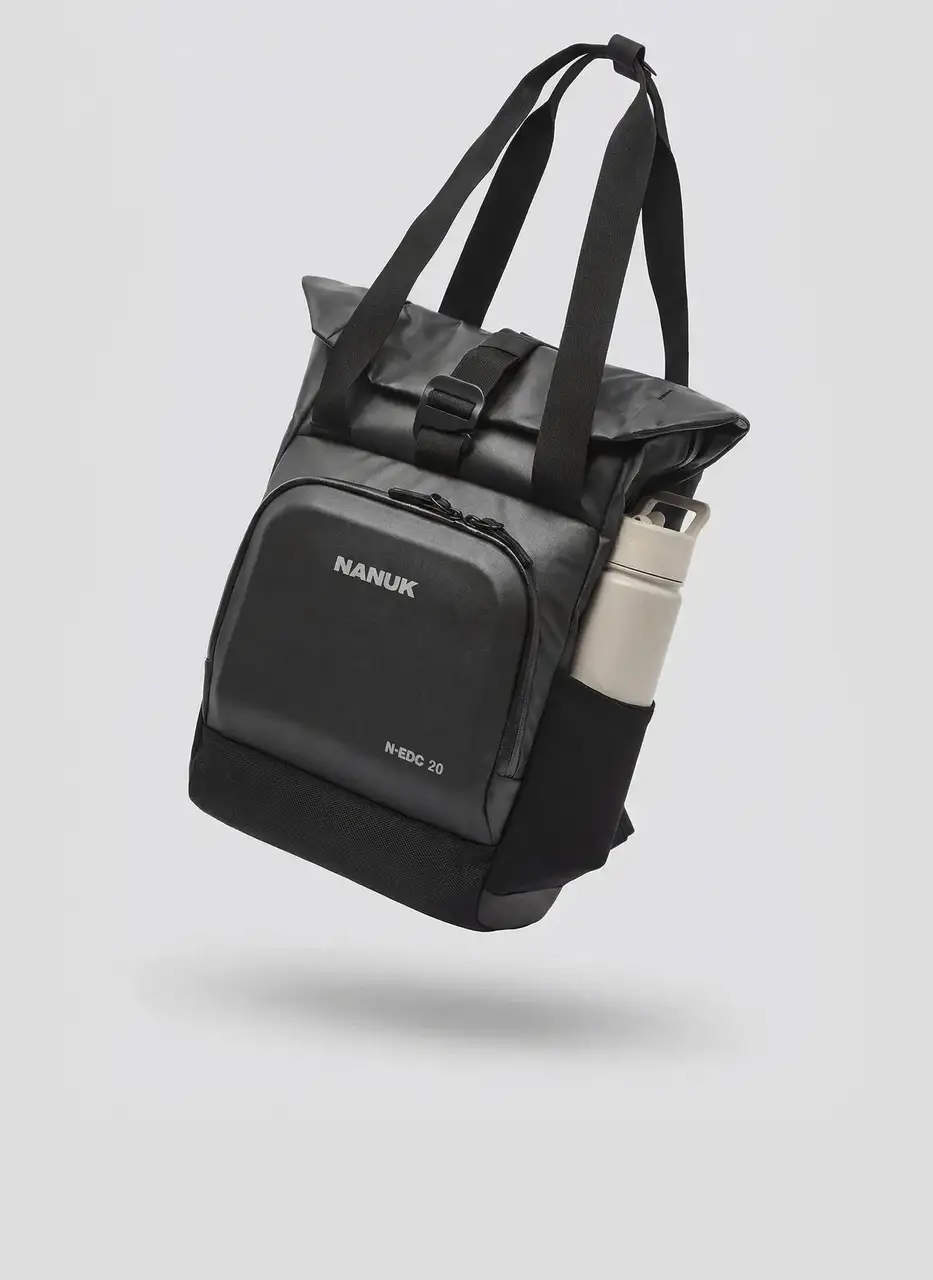 A black JunZhiJia N-EDC 20 bag with a roll-top buckle closure and a water bottle in its side pocket is presented floating against a light gray background, highlighting its functionality among JunZhiJia bags and cases.