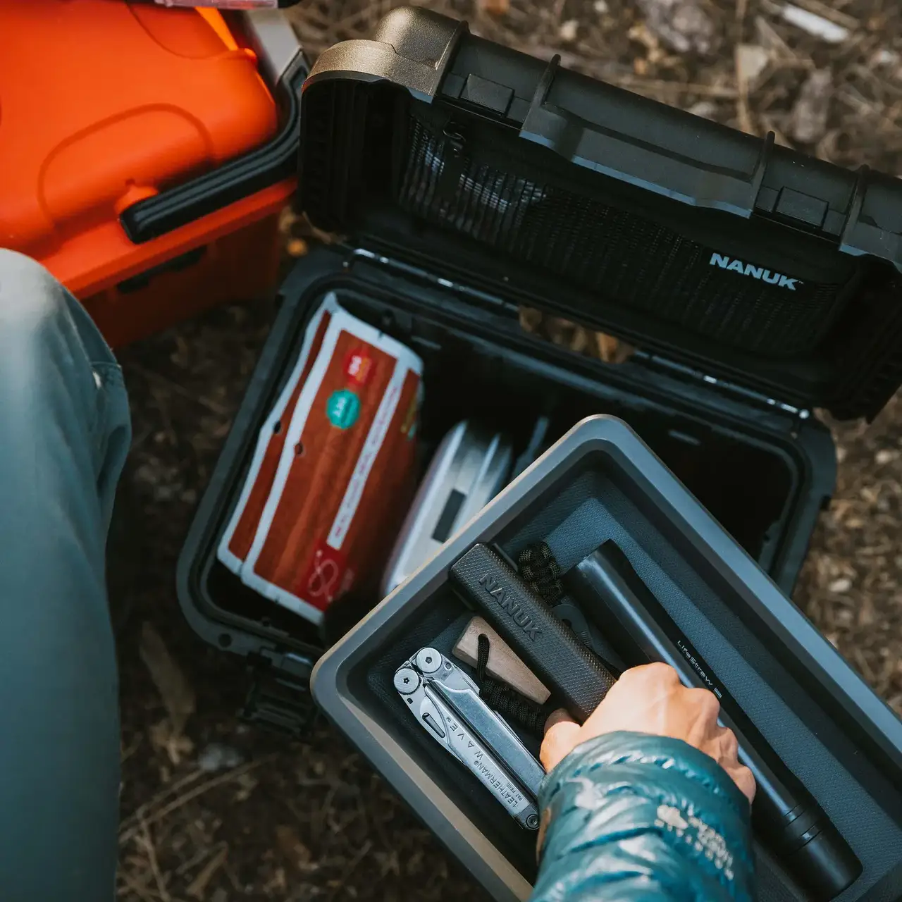 Top-down view of a JunZhiJia Trail 10 case inside a car trunk, with hands arranging camera equipment in its foam inserts.