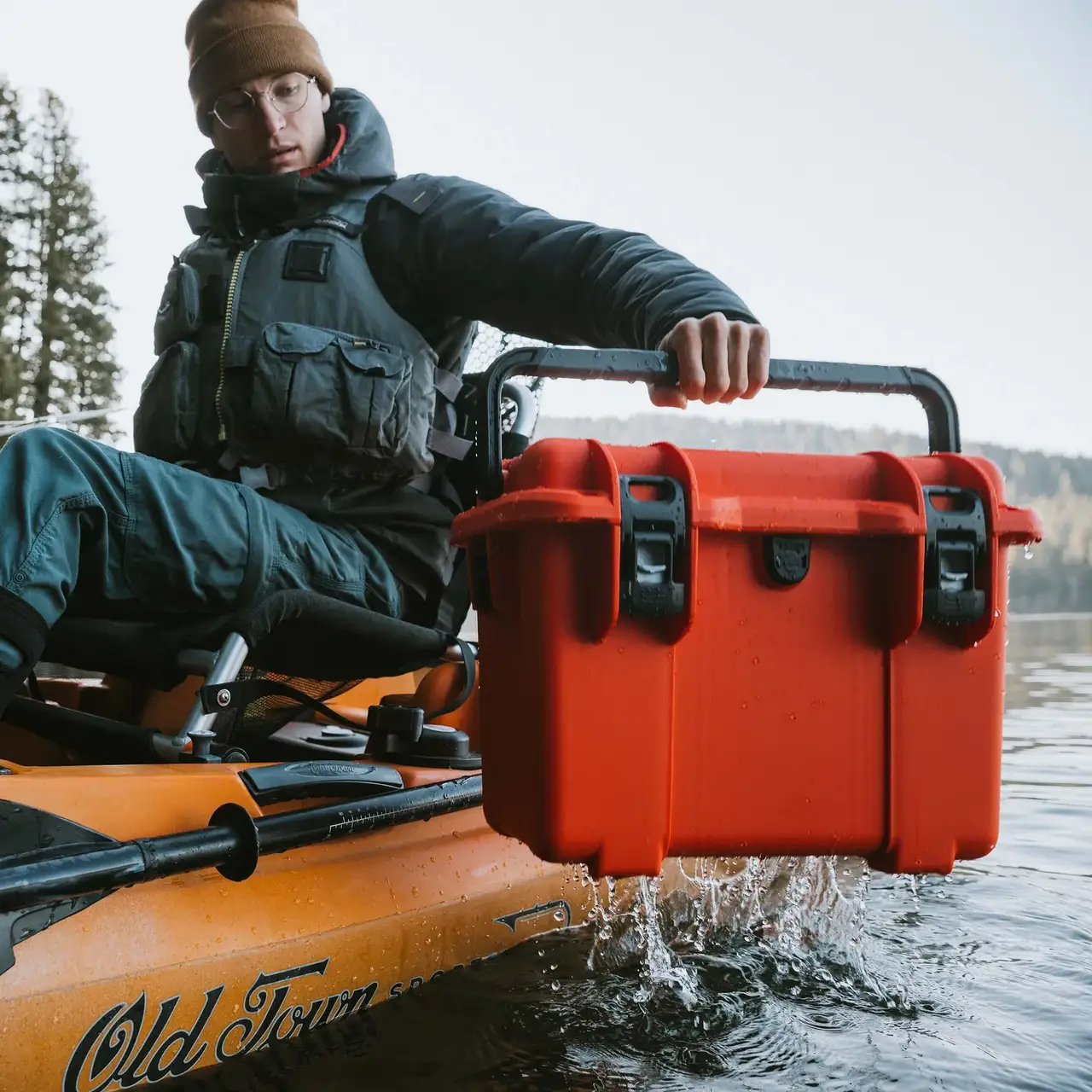Person fishing from a kayak on a lake with a closed orange JunZhiJia Trail 15 protective case beside them.