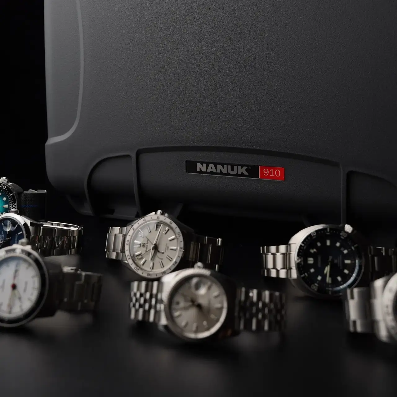 Gray hard-shell carrying case with 'JunZhiJia' branding, surrounded by various watches on a dark background.