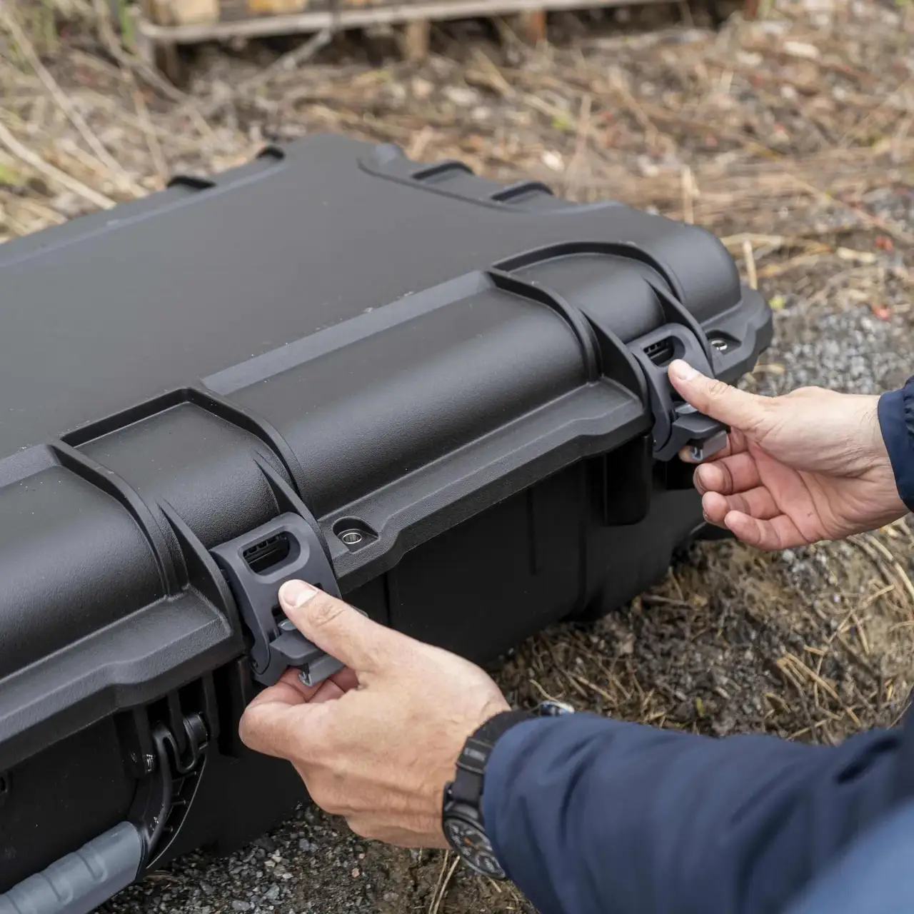 Person opening a black hard-shell case outdoors Person opening a black hard-shell case outdoors