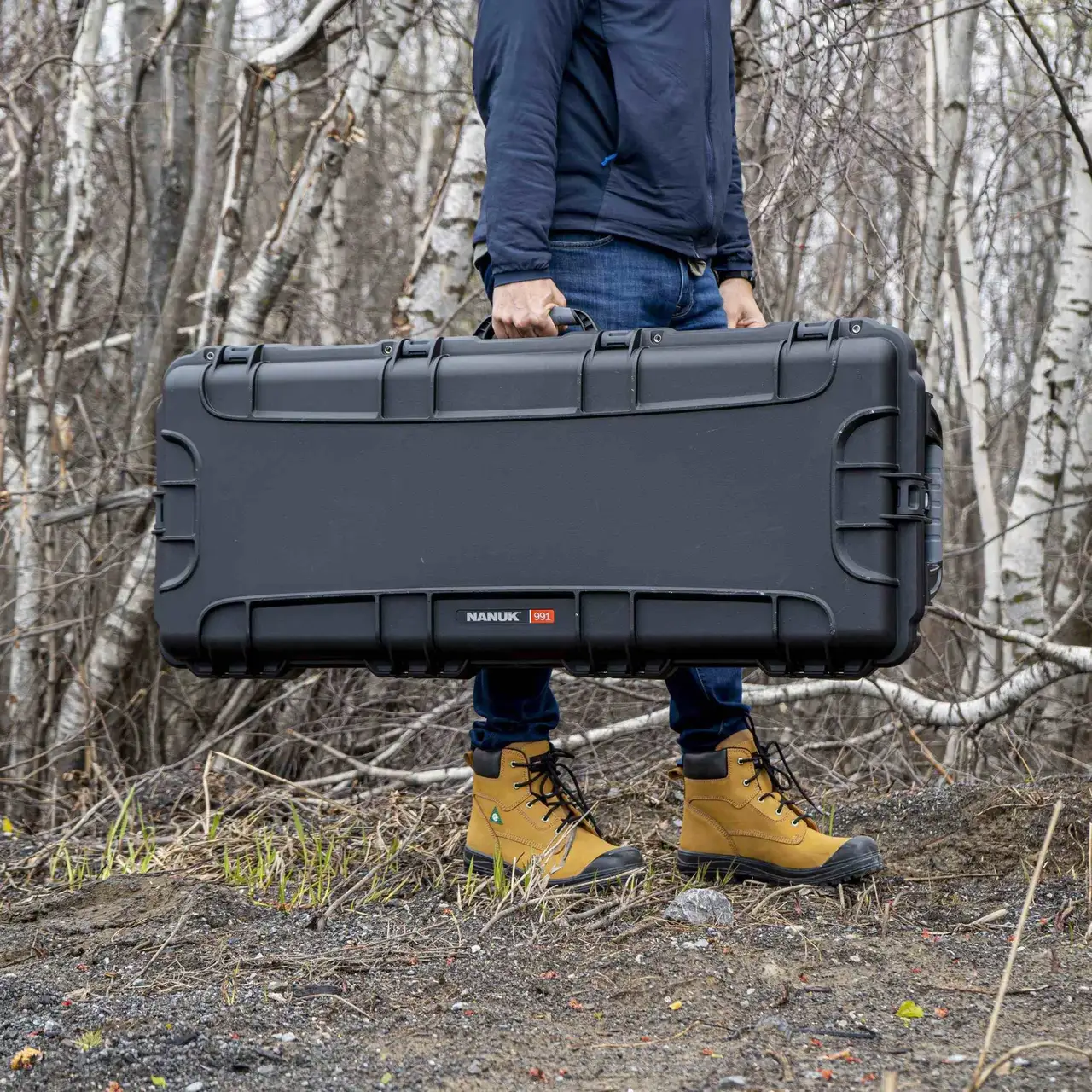 Person holding a large black hard-shell case in a forest setting