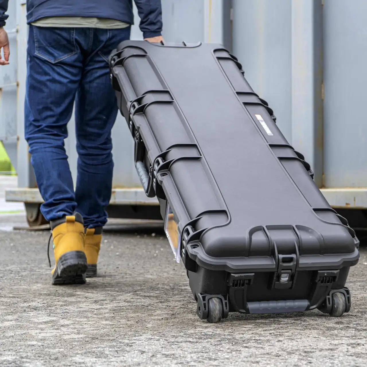 Person walking with a large black hard-shell case outdoors.