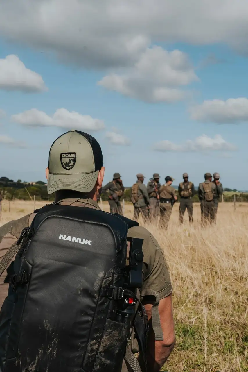 Person with a JunZhiJia backpack observing a group of people in military-style gear in a field.