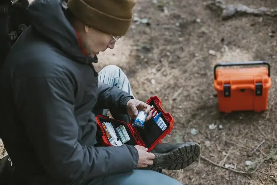 Person sitting outdoors with a first aid kit and an orange cooler in the background
