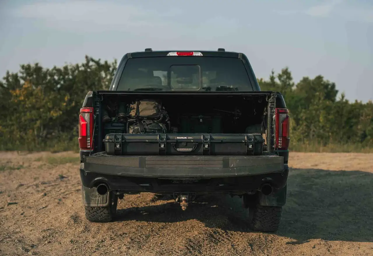 Back view of a black pickup truck with an open bed on a dirt road.