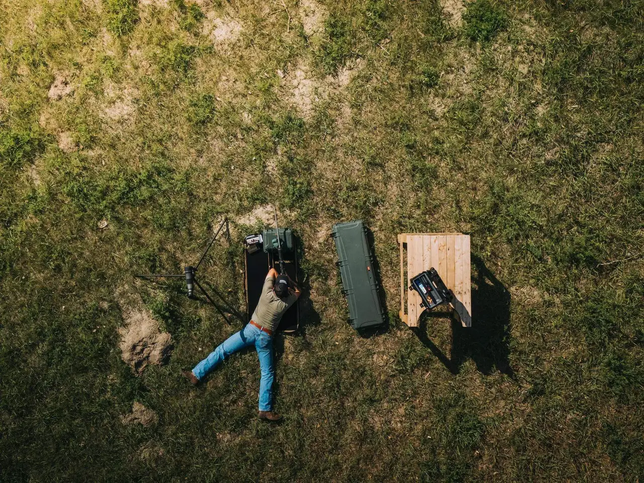 Person lying on grass next to a backpack and wooden box in an open field
