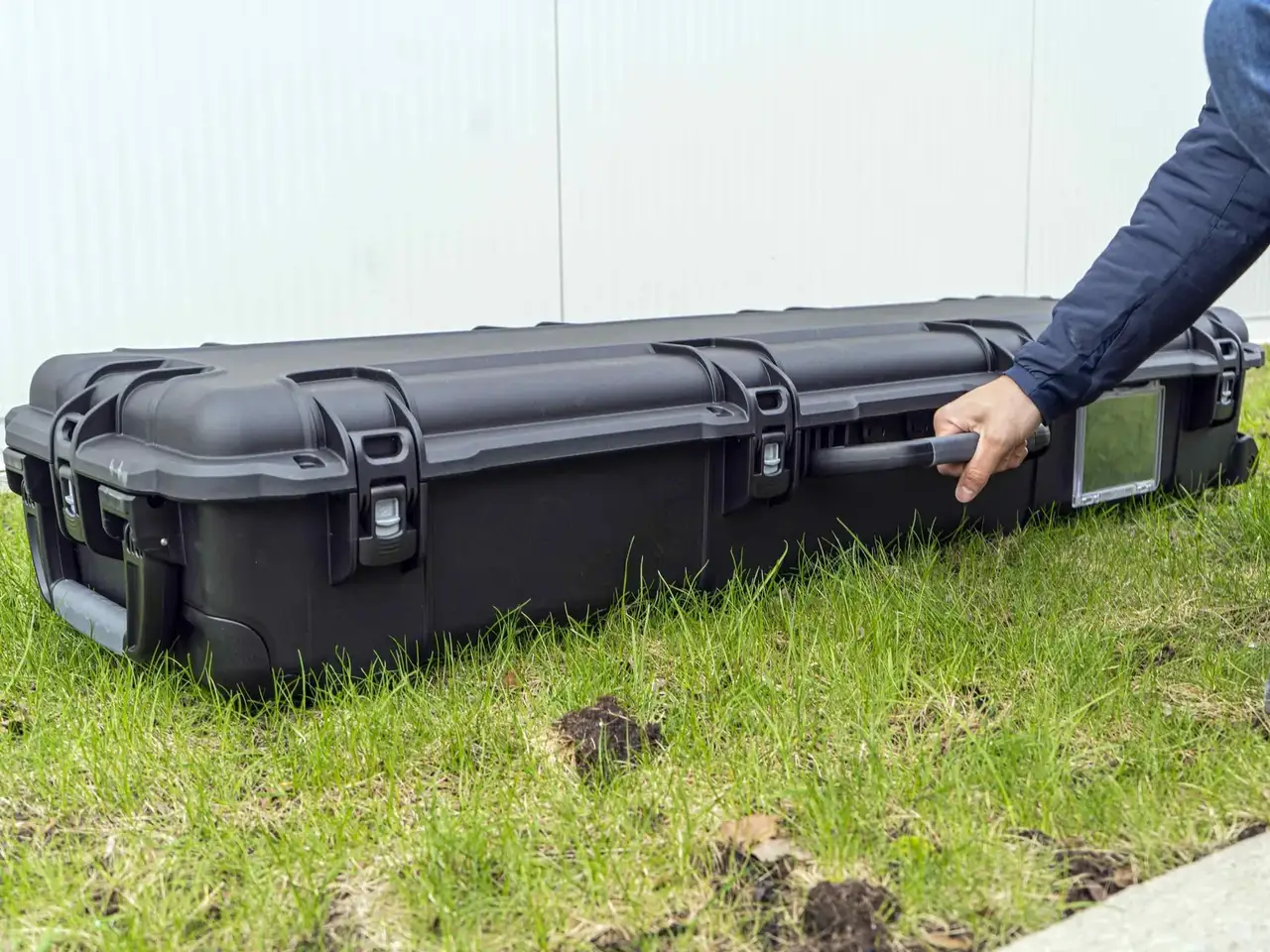 Person opening a large black hard-shell case on grass