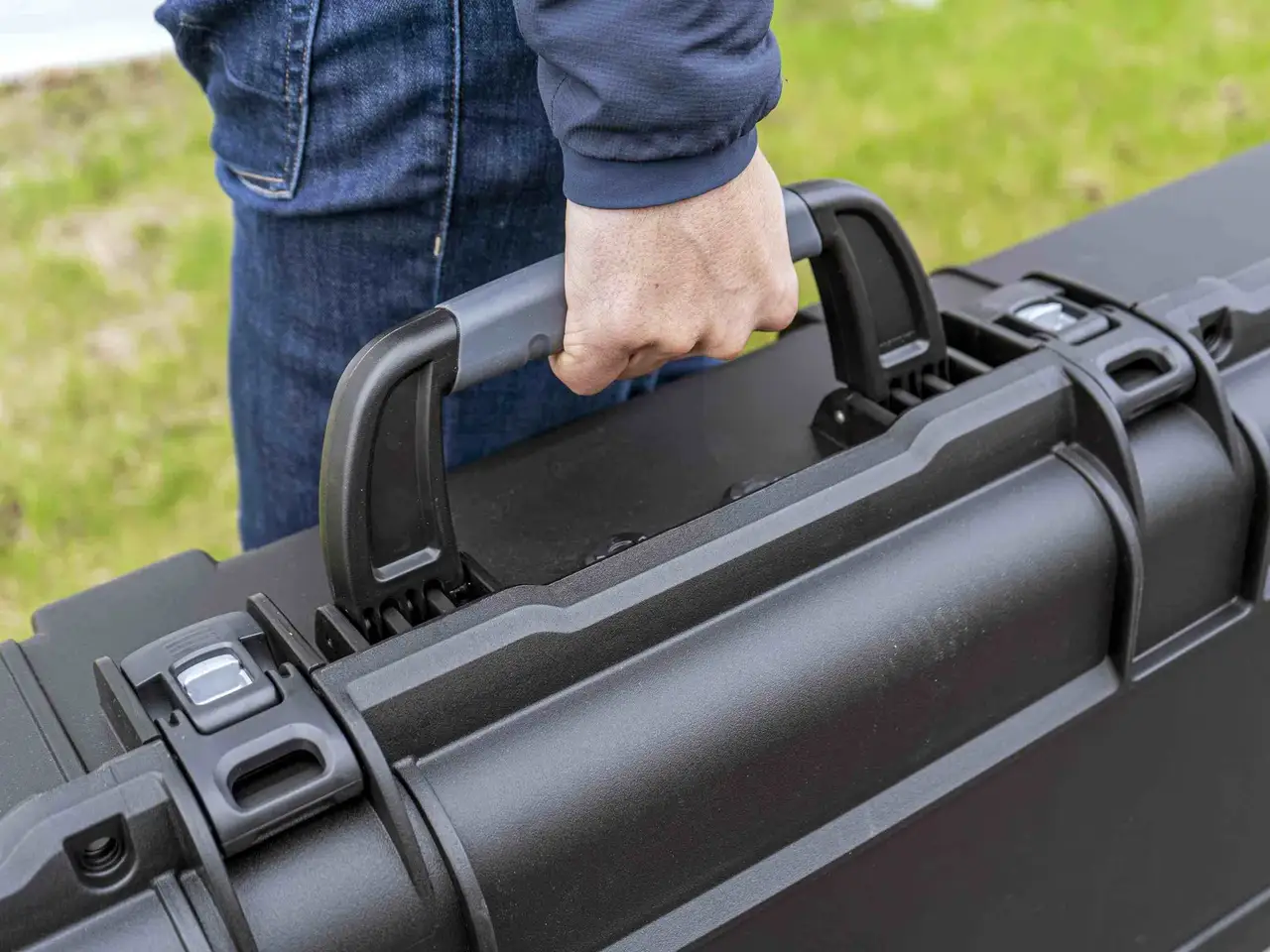 Person holding a black hard-shell suitcase outdoors