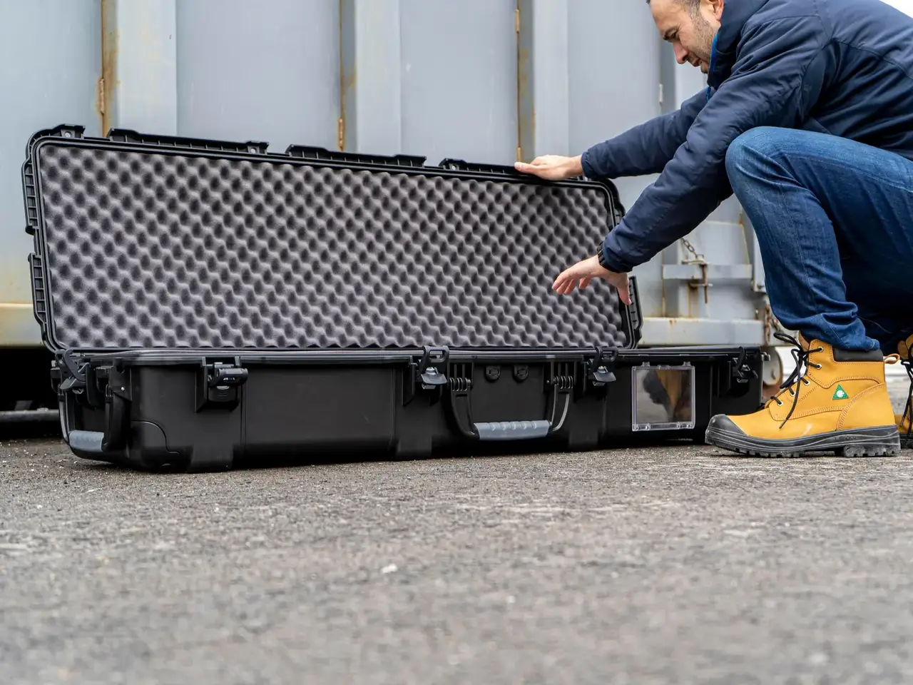 Person opening a large black and gray foam-lined case outdoors.