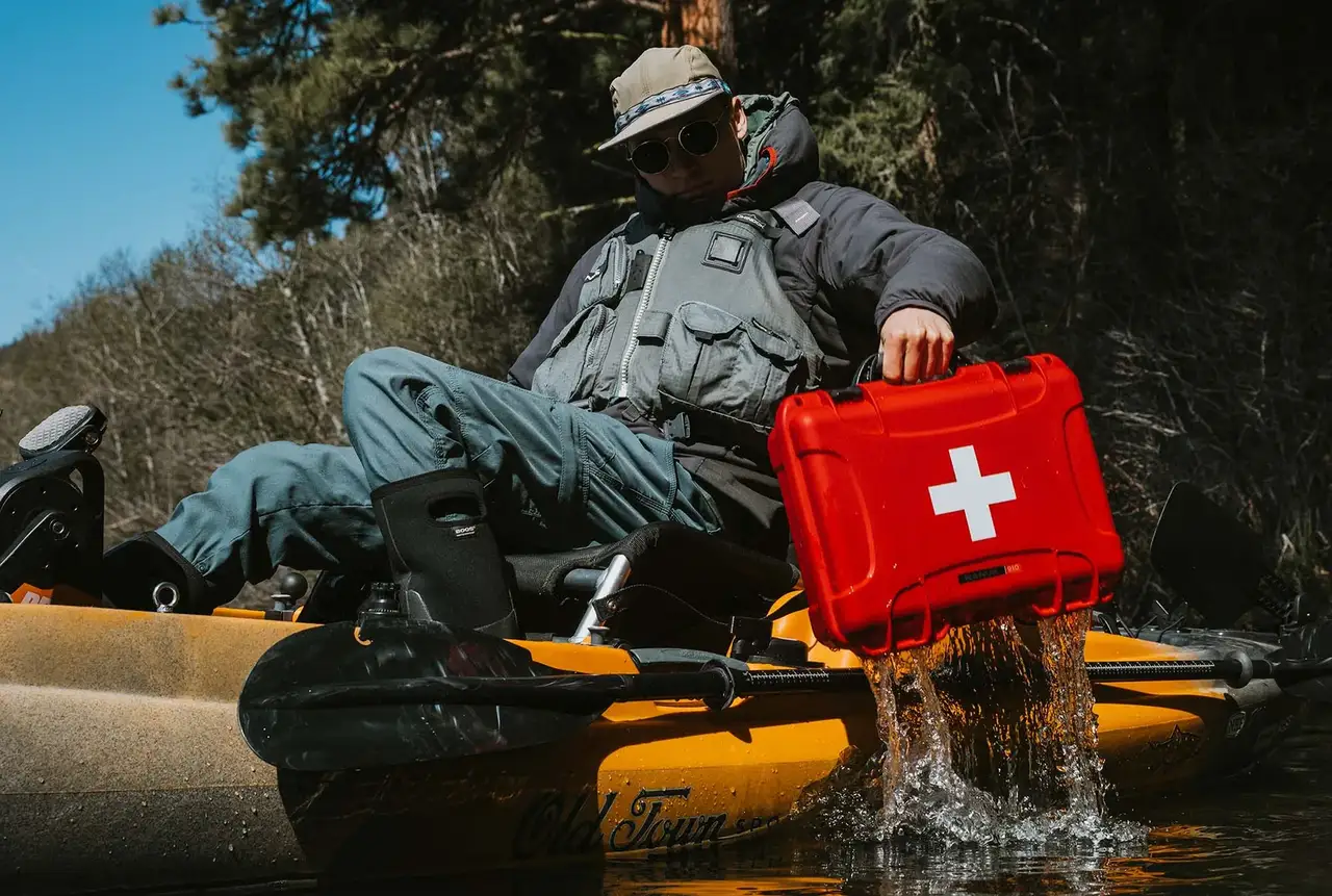 A rugged red JunZhiJia First Aid Case rests on a yellow kayak beside two adventurers preparing for a water journey.