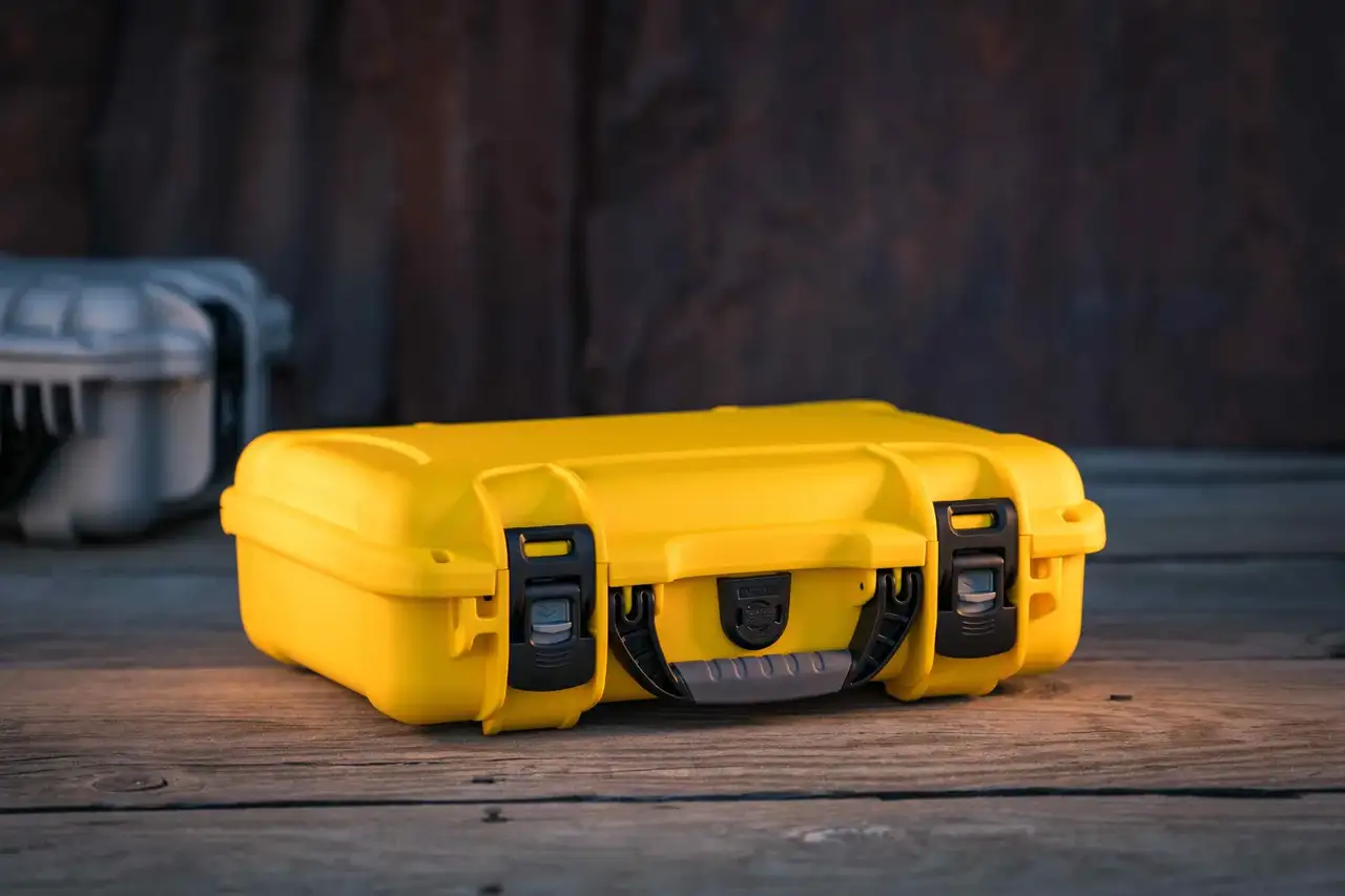 The JunZhiJia 910 protective hard case in bright yellow, resting on a textured wooden surface with a rugged industrial backdrop.