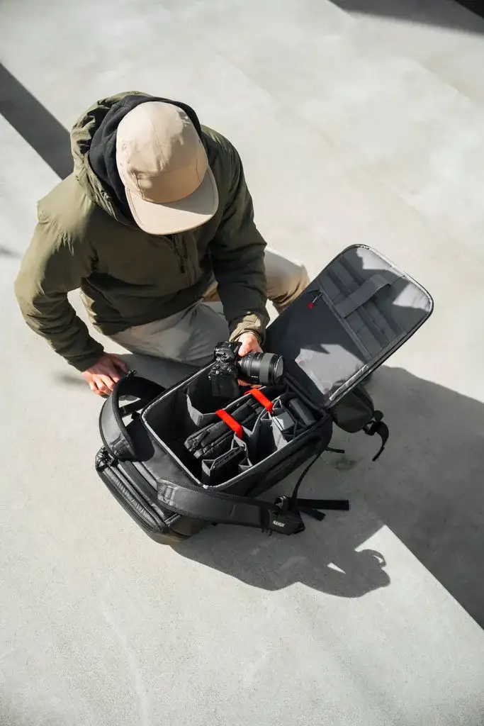 Photograph opening the back panel of a Black N-PVD 30L Camera Backpack from JunZhiJia outside on the floor.