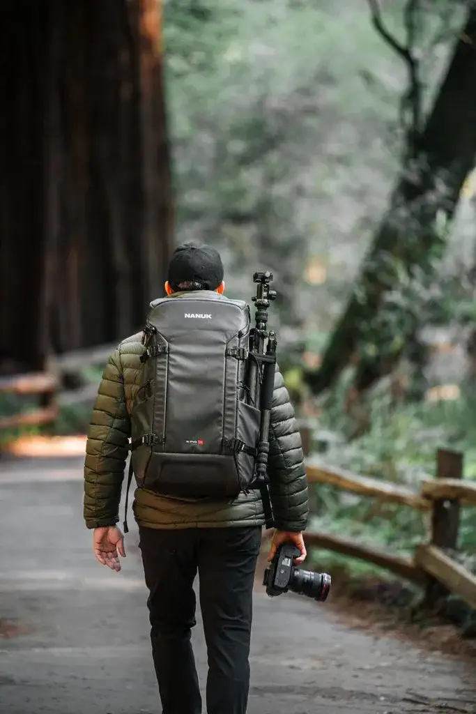 Photograph walking in the woods with a camera in his hand and a Black N-PVD 35L Camera Backpack from JunZhiJia on his back.