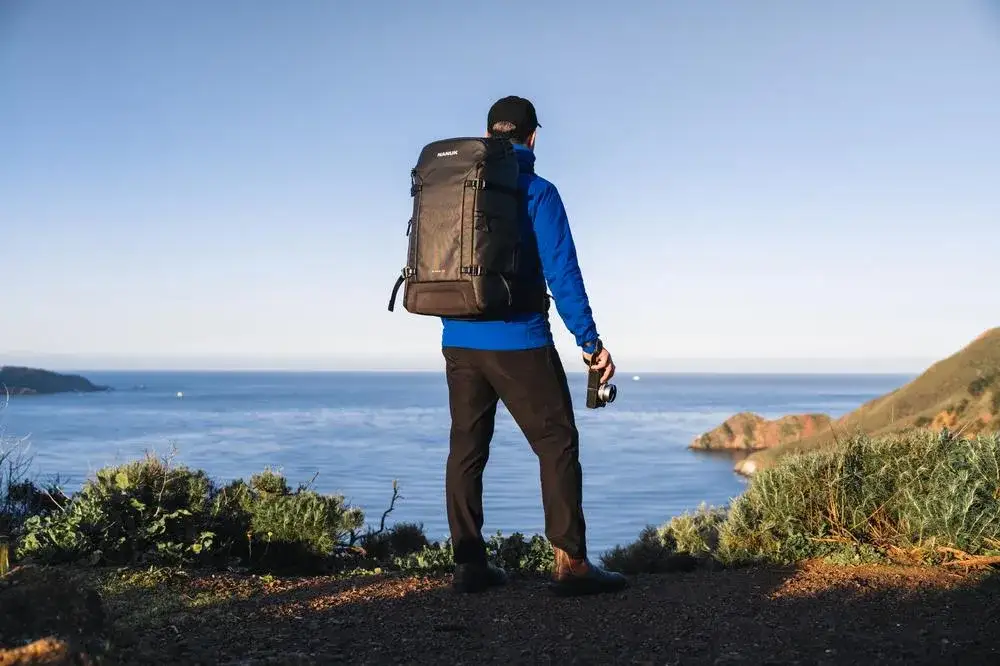 Photograph taking a picture of the ocean with a Black N-PVD 35L Camera Backpack from JunZhiJia on his back.