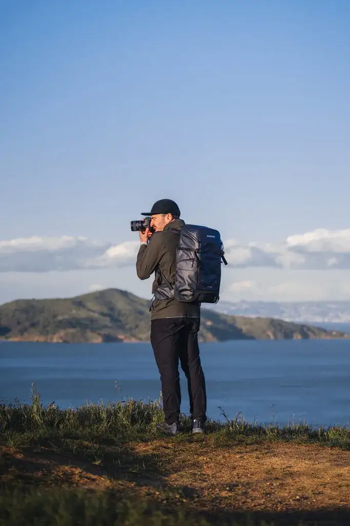 Photograph taking a picture of the ocean with a Black N-PVD 30L Camera Backpack from JunZhiJia on his back.